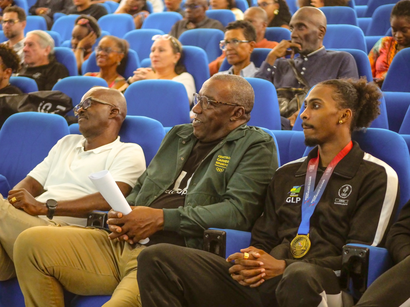 Des personnes réunies dans un auditorium ; au premier plan, l’une porte une médaille.