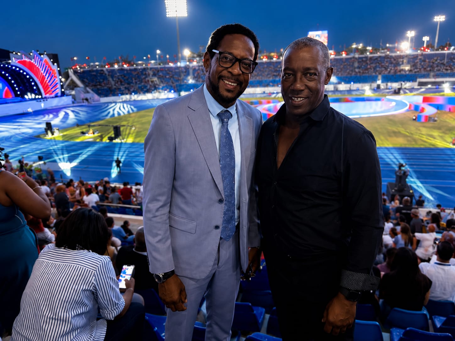Deux personnes dans les tribunes d’un stade éclairé, devant une cérémonie.